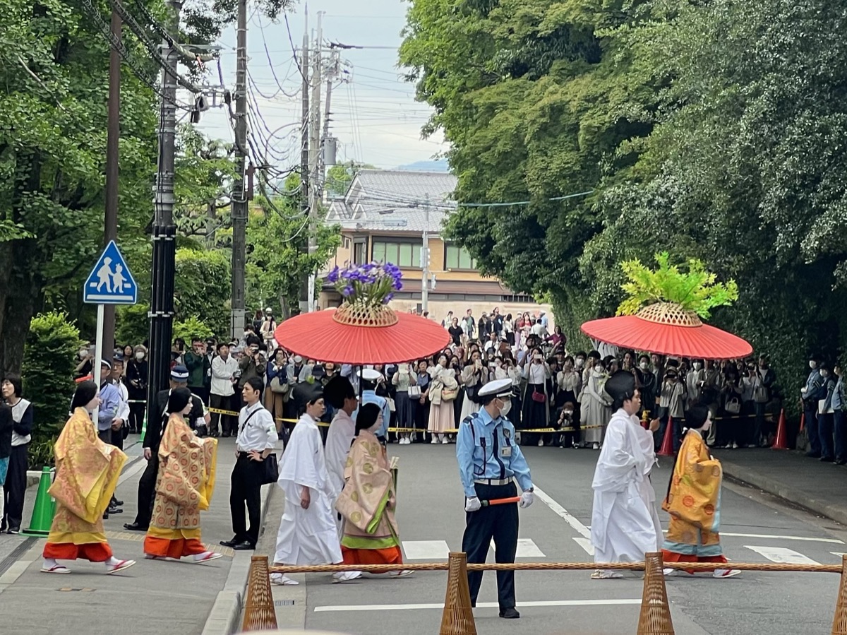 Aoi Matsuri participants in Heian-era court costume walking under red parasols with crowds watching