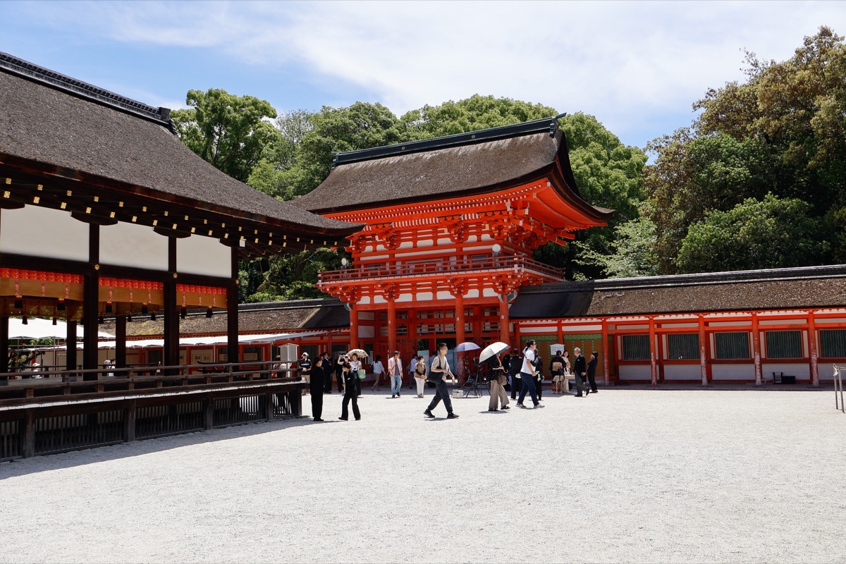 Shimogamo Shrine courtyard with vermillion romon gate, visitors, and surrounding forest under blue sky