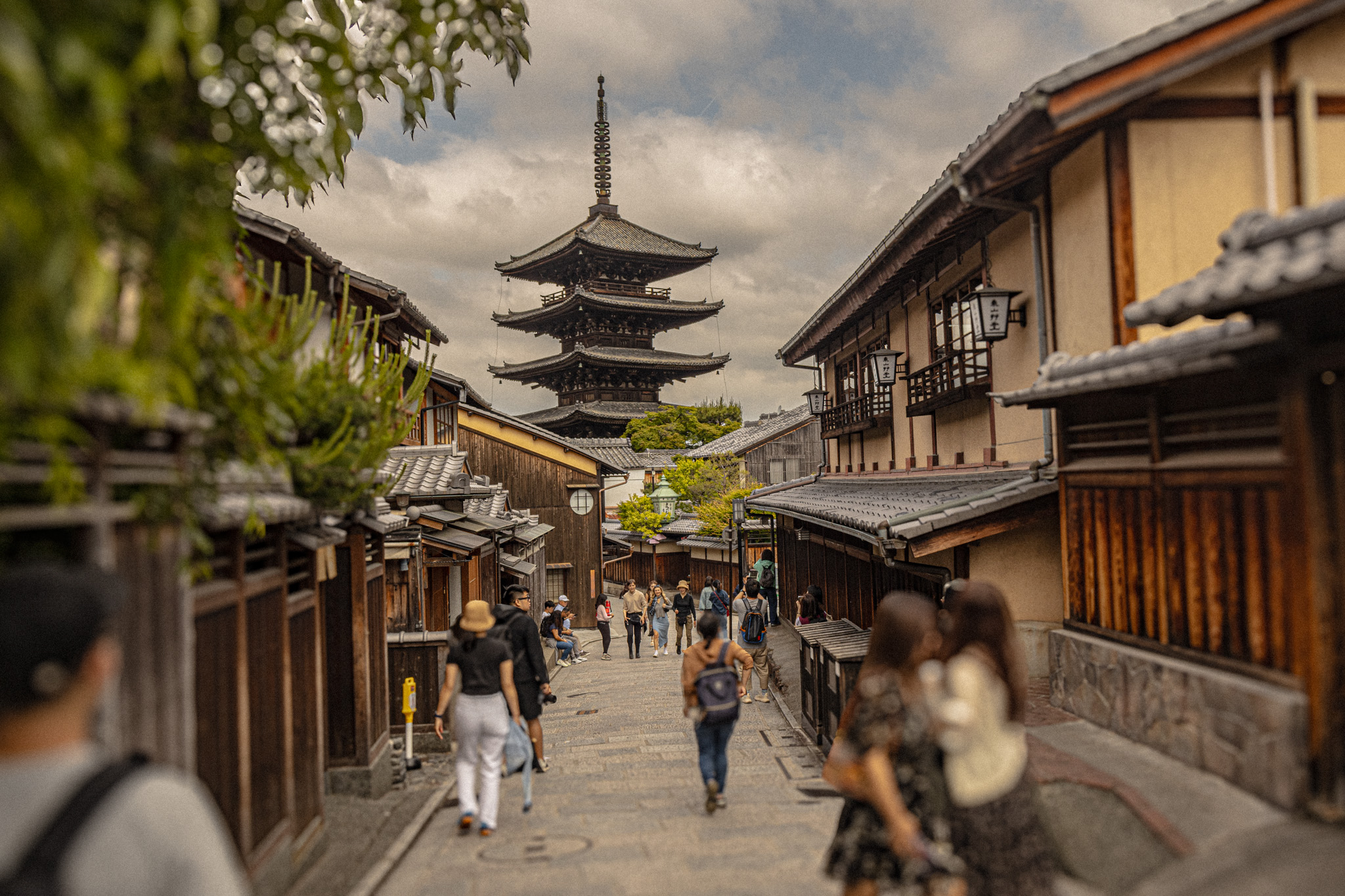 Visitors walking through Higashiyama backstreets with Yasaka Pagoda rising above traditional wooden buildings in Kyoto