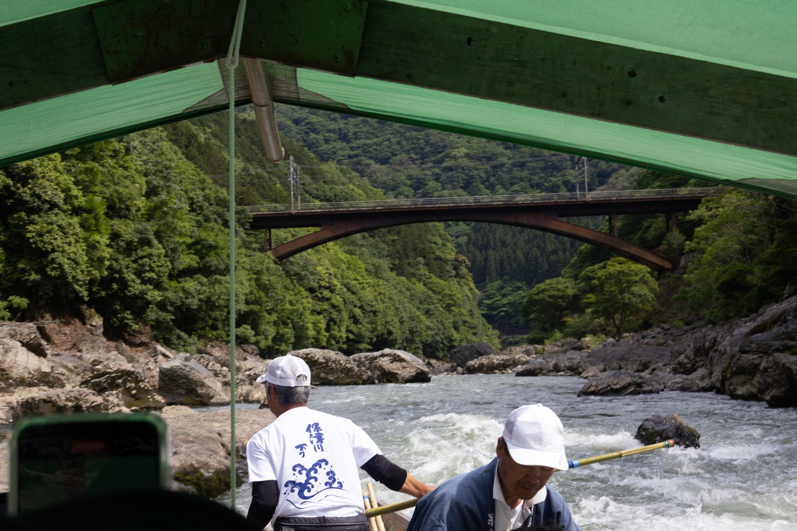 Wooden Hozugawa river boat with boatmen poling through mild rapids in the gorge